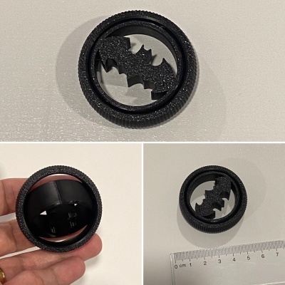 Objeto circular preto com textura de pneu e símbolo de morcego no centro