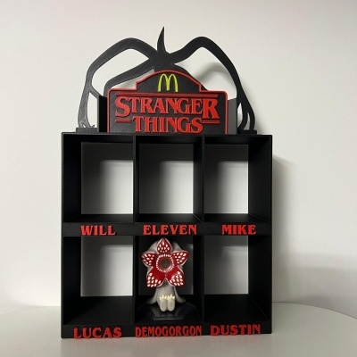 Expositor preto com seis cubos, nomes vermelhos e logo Stranger Things no topo