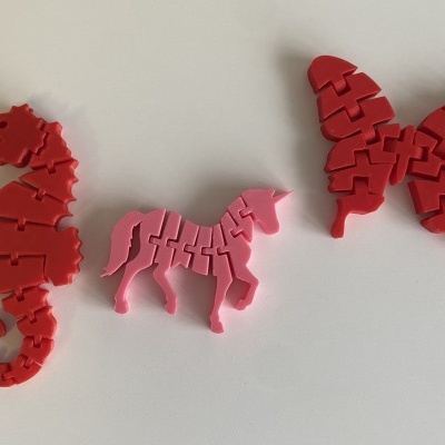 Três puzzles pequenos em formas de cavalo-marinho, cavalo e borboleta em plástico vermelho e rosa