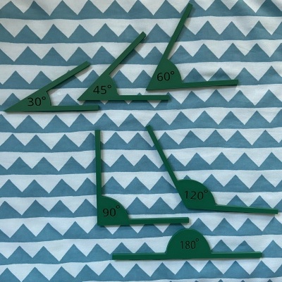 Conjunto de réguas de plástico verde com ângulos marcados sobre tecido com padrão de triângulos.