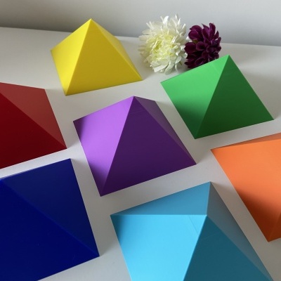 Sete pirâmides coloridas em papel com duas flores artificiais ao fundo