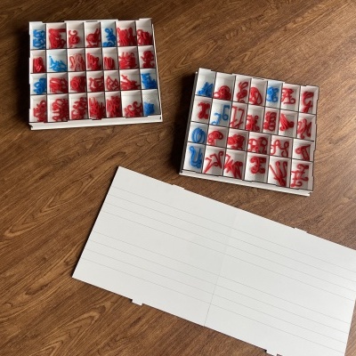 Caixas pequenas com peças numéricas vermelhas e azuis e folha branca com linhas sobre mesa de madeira.