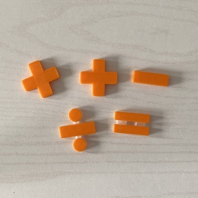 Símbolos matemáticos de plástico laranja sobre uma superfície clara com padrão de madeira