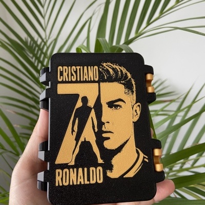 Caixa preta com imagem dourada de Cristiano Ronaldo e fundo de plantas verdes
