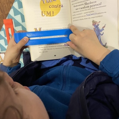 Criança a ler livro com régua azul em cenário com almofadas e padrão azul