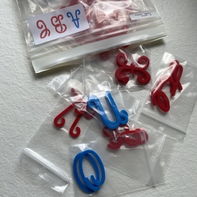 Letras de plástico vermelhas e azuis em sacos transparentes sobre superfície branca