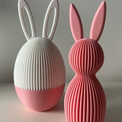 Objetos decorativos em forma de coelhos com texturas estriadas, um branco e rosa, outro só rosa