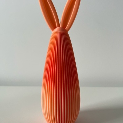 Objeto decorativo laranja com textura e orelhas, sobre superfície branca