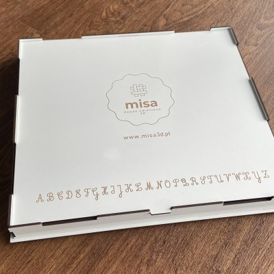 Caixa branca com logótipo misa e alfabeto impresso em papelão sobre mesa de madeira