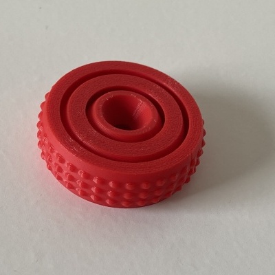 Peça plástica circular vermelha com textura e ranhuras sobre fundo branco