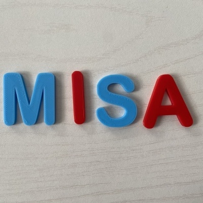 Letras magnéticas MISA em azul e vermelho sobre superfície cinza clara textura madeira