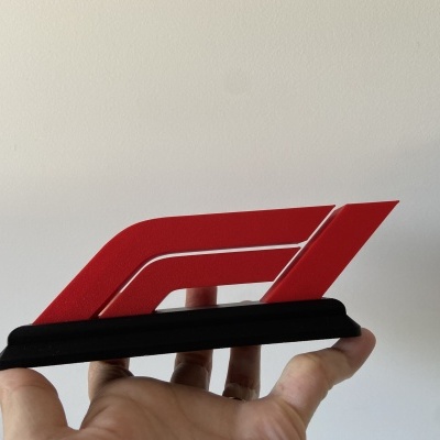 Logótipo vermelho e preto da Fórmula 1 em material plástico segurado por uma mão