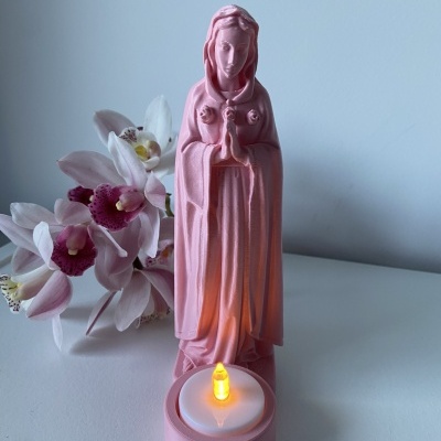 Estátua rosa de figura feminina com vela LED e flores ao fundo