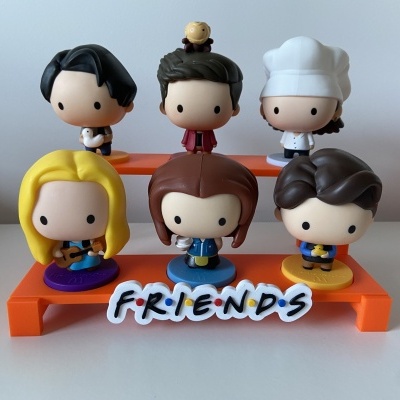 Conjunto de seis bonecos de plástico dos amigos da série Friends sobre suporte laranja com texto FRIENDS.