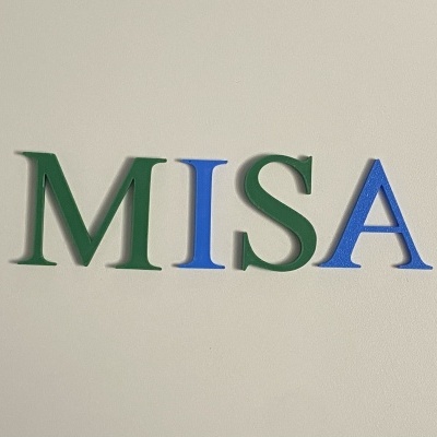 Letras recortadas 'MISA' em verde e azul na parede branca