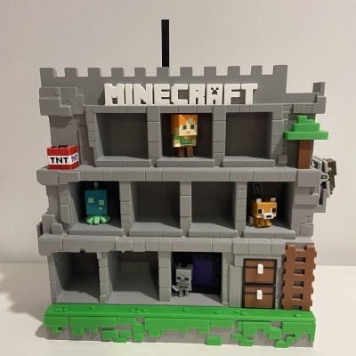 Brinquedo de construção Minecraft cinzento com figuras coloridas e detalhes de castelo em fundo branco.