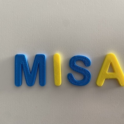 Letras de plástico azul e amarelo formando MISA numa superfície branca