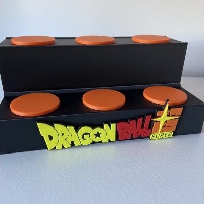 Caixa preta com letras coloridas Dragon Ball Super e discos laranja em cima.