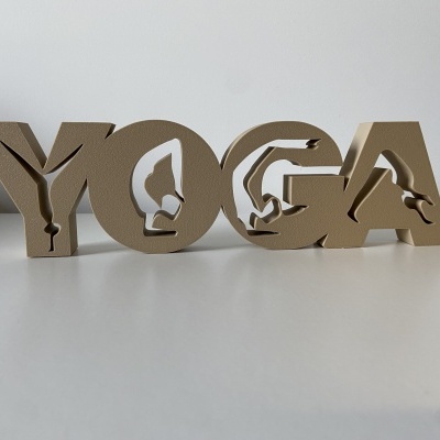 Objeto decorativo em madeira com a palavra YOGA e silhuetas de pessoas em poses de yoga.