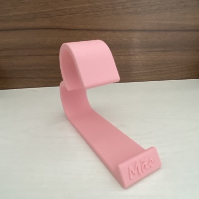 Suporte para telemóvel rosa com o texto 'Mãe' sobre superfície branca e fundo de madeira