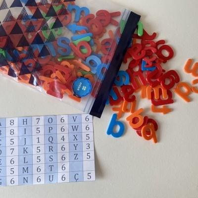 Letras magnéticas coloridas, saquinho estampado e folha com tabela alfanumérica sobre superfície branca