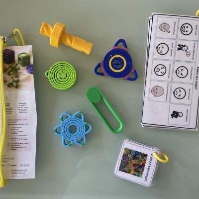 Fidgets coloridos e cartões com expressões e frases em português dispostos sobre uma superfície