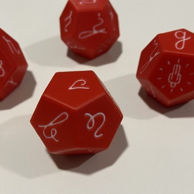 Quatro dados vermelhos de 12 faces com símbolos e números brancos sobre superfície branca.