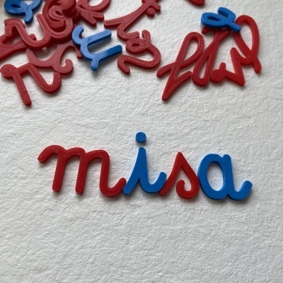 Letras decorativas em madeira vermelhas e azuis formando a palavra misa sobre fundo branco texturado