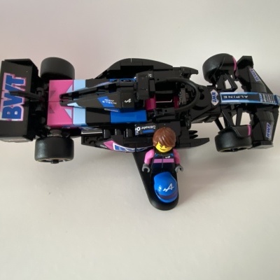 Miniatura carro de Fórmula 1 preto com azul e rosa e figura de brinquedo com capacete