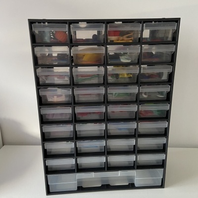 Organizador preto com várias gavetas transparentes contendo objetos pequenos