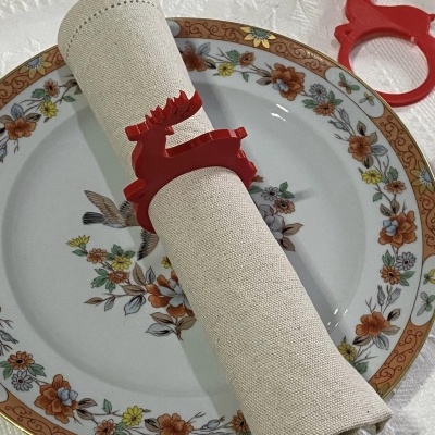 Guardanapo bege com anel de rena vermelho sobre prato floral em toalha branca