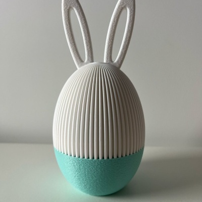 Objeto decorativo em forma de ovo com orelhas brancas e base verde água