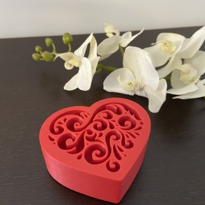 Caixa vermelha em forma de coração com desenho recortado e flores brancas ao fundo