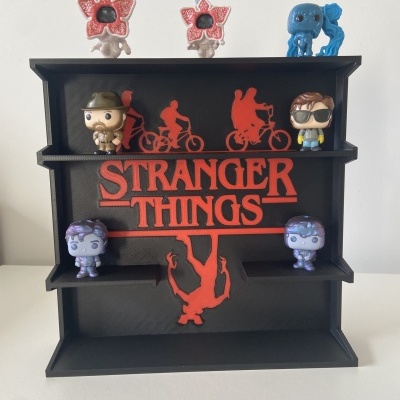 Estante preta com texto vermelho STRANGER THINGS e figuras colecionáveis de personagens em várias cores.