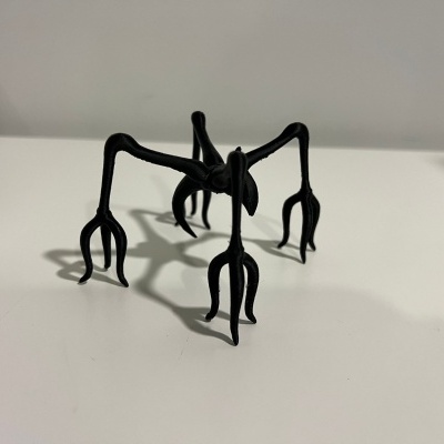 Figura decorativa preta com pernas longas e garras sobre mesa branca