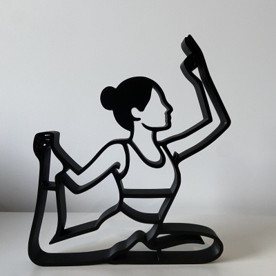 Escultura de metal preta representando mulher numa pose de yoga.