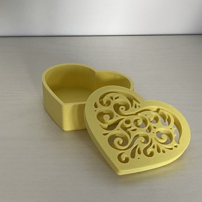 Caixa coração amarela com tampa ajourada decorativa aberta sobre superfície clara