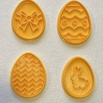 Quatro moldes amarelos em forma de ovo com padrões de laço, ondas, zig-zag e coelho