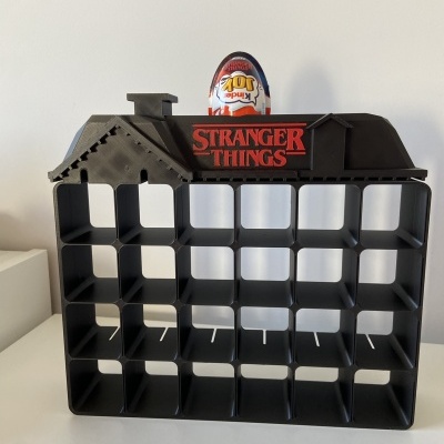 Organizador preto em forma de casa com compartimentos e texto Stranger Things, ovo Kinder Joy em cima.