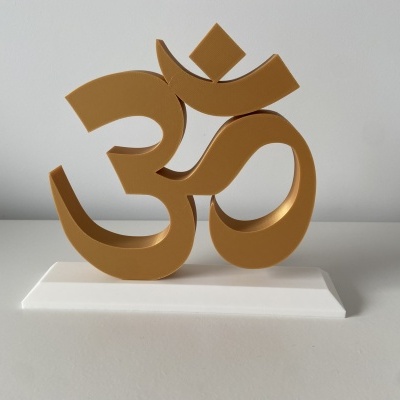 Escultura dourada do símbolo Om sobre base branca