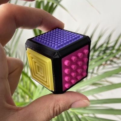 Cubóide de plástico com lados coloridos e texturas diferentes segurado por dedos.
