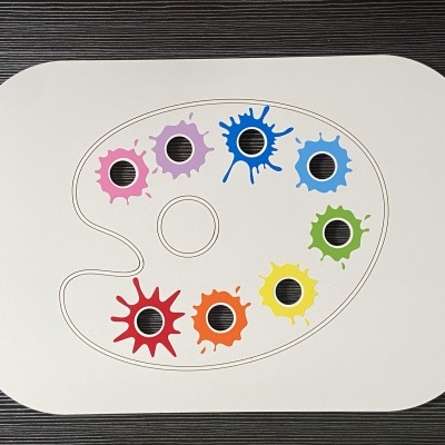 Prato cerâmico formato paleta de pintor com tintas coloridas e sensores pretos sobre fundo madeira preta.