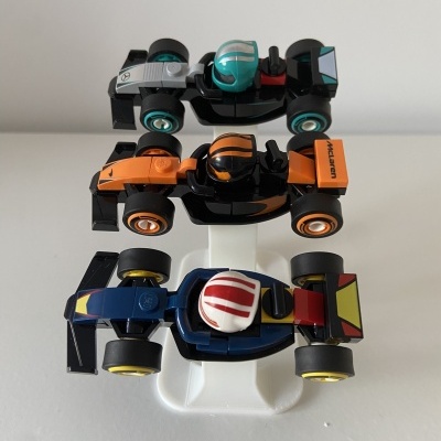 Três carrinhos de corrida em miniatura em diferentes cores com suporte branco