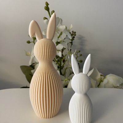 Dois coelhos decorativos bege claro e branco com textura canelada sobre superfície branca