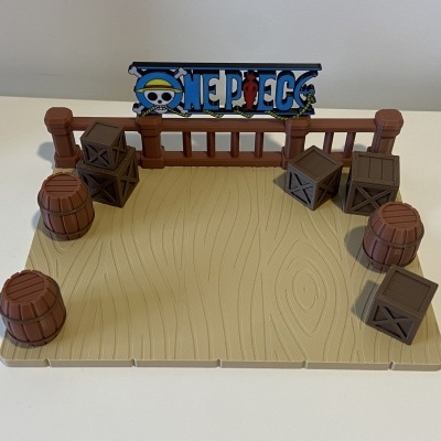 Base de brinquedo simulando madeira com caixas, barris e placa One Piece colorida