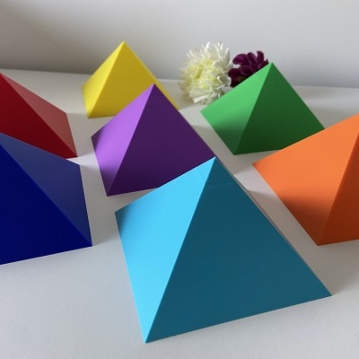 Pirâmides de papel coloridas sobre uma superfície branca com flores ao fundo