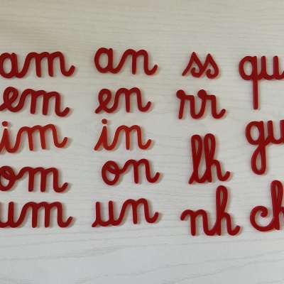 Peças vermelhas em formato de letras ligadas sobre superfície clara.