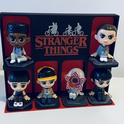Figuras colecionáveis dos personagens de Stranger Things em suporte preto com fundo vermelho e texto