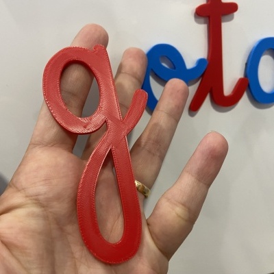 Letra g vermelha em plástico segurada por mão com fundo branco e outras letras