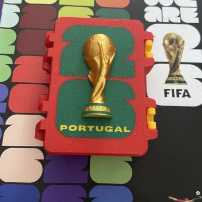 Álbum e objeto vermelho com troféu dourado e frase Portugal em fundo colorido.